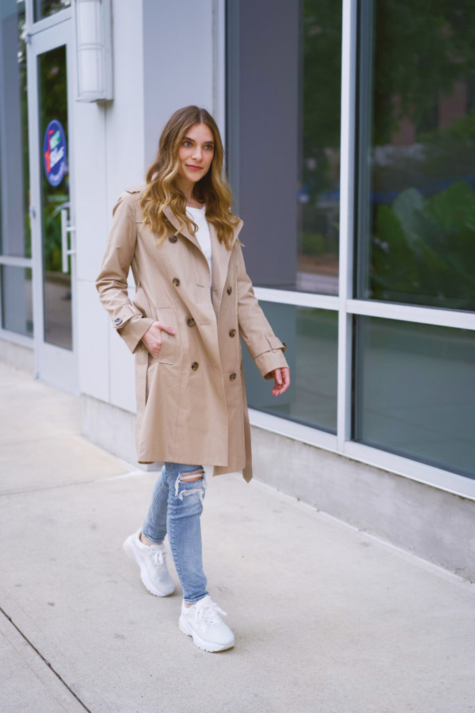 Woman wearing white sneakers, jeans, and a trench coat